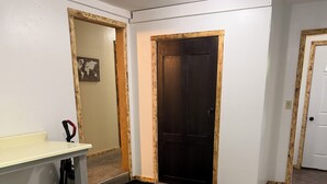 Un corridoio con una porta in legno, una panca bianca, un tappetino nero e un tappeto decorato.