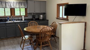 Una cucina con un tavolo da pranzo, sedie, un televisore e un orologio appeso al muro.