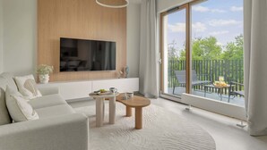 Uma sala de estar moderna com uma televisão de tela plana, um sofá, uma mesa de centro e uma varanda com mobiliário externo.