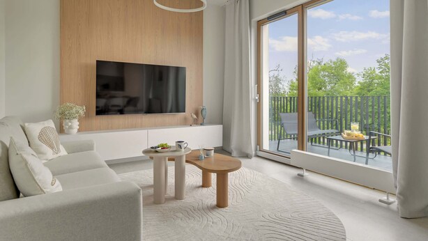 A modern living room with a flat-screen TV, a sofa, a coffee table, and a balcony with outdoor furniture. - Nowe Kolibki 23 | 2 Bedrooms | Parking (Gdynia)