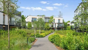 A pathway leading to modern residential buildings with balconies, surrounded by greenery. - Nowe Kolibki 23 | 2 Bedrooms | Parking (Gdynia)