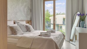 A modern bedroom with a large bed, a mirror, and a view of the outside. - Nowe Kolibki 23 | 2 Bedrooms | Parking (Gdynia)