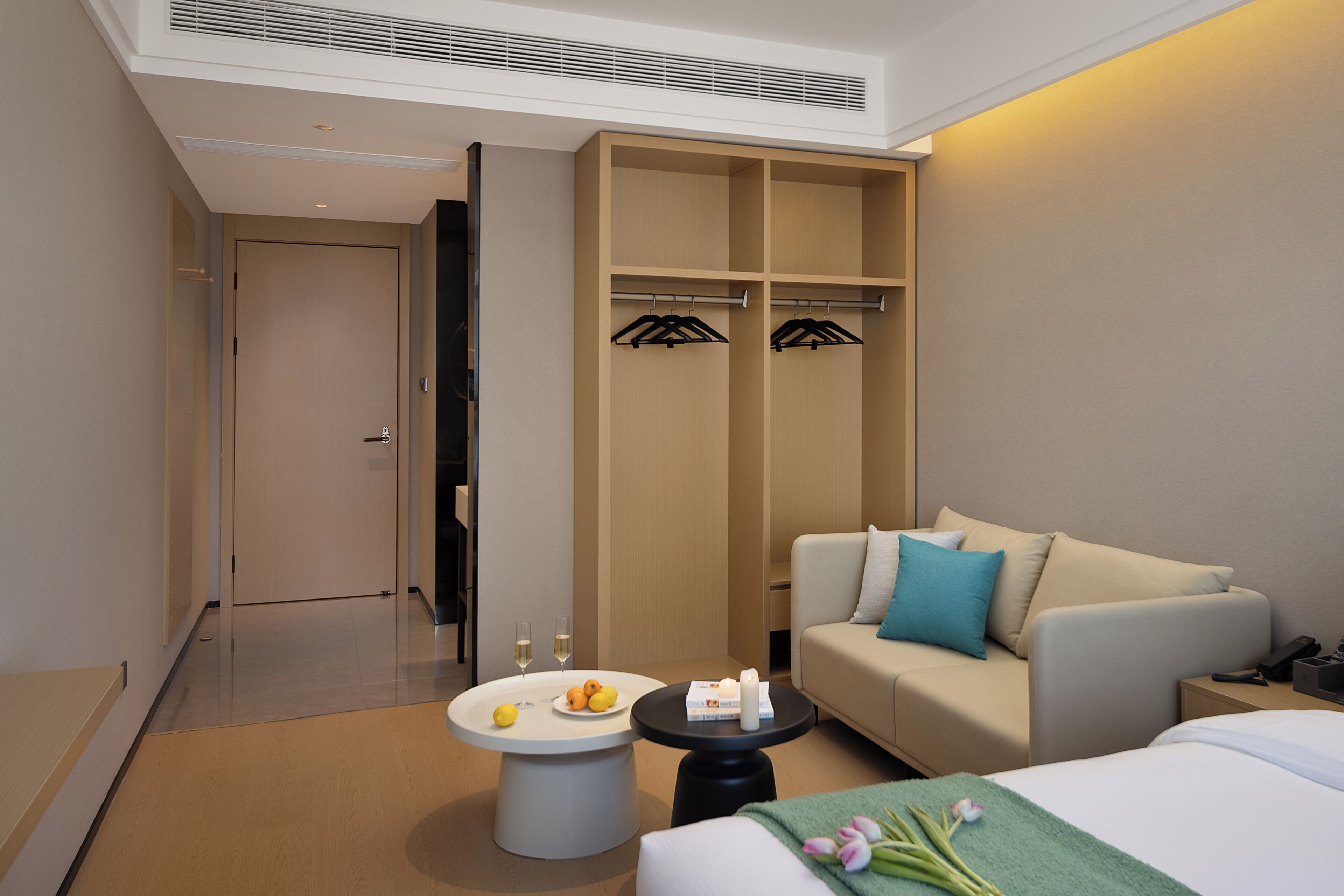 Ein Hotelzimmer mit Bett, einer Couch, einem Tisch mit Früchten und Gläsern, einem Kleiderschrank und einer Tür zu einem weiteren Raum.