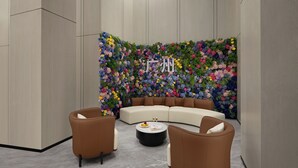 Un salon moderne avec un canapé incurvé, deux fauteuils et une table basse. Un décor mural floral aux couleurs vives se trouve derrière l’espace détente.