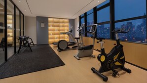 Une salle de sport moderne équipée de matériel d’exercice, dotée d’un espace détente et offrant une vue sur la ville grâce à de grandes fenêtres.