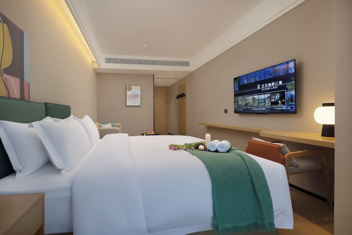 Una habitación de hotel con cama, escritorio, televisor y un cuadro en la pared.