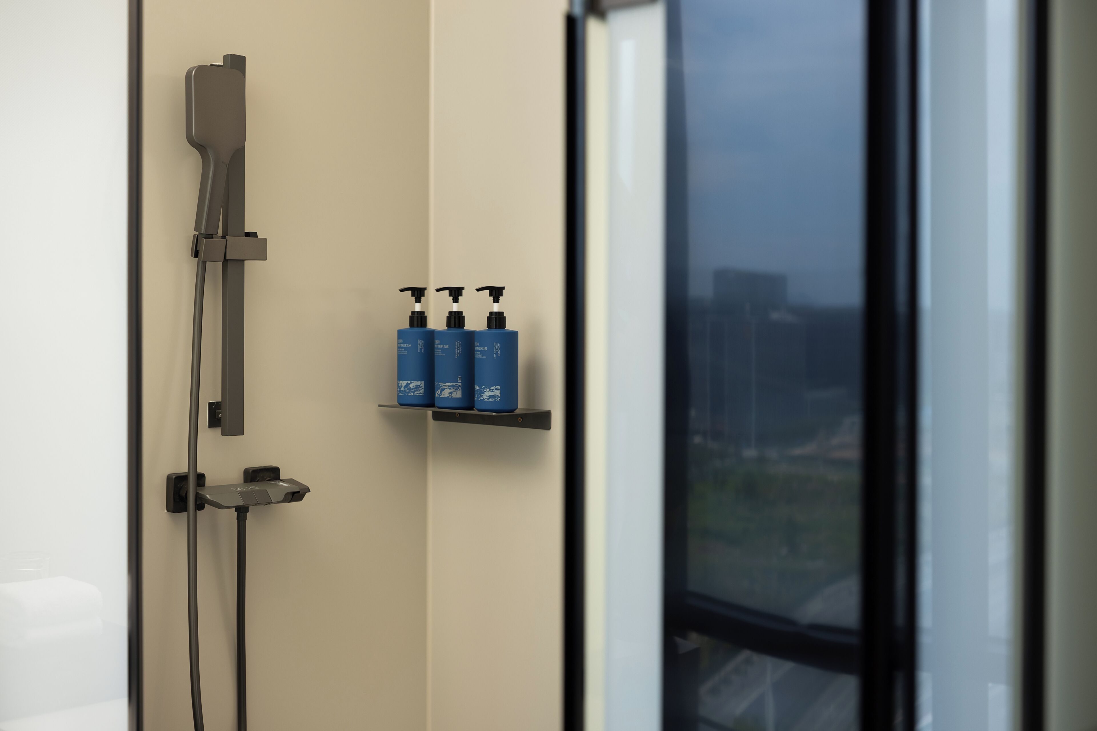 A shower with a handheld showerhead, a wall-mounted faucet, and a shelf with three bottles.