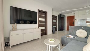 Ein modernes Wohnzimmer mit einem grauen Sofa, einem kleinen runden Tisch und einem an der Wand montierten Flachbildfernseher.