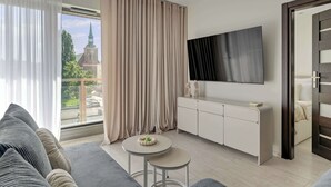Ein modernes Wohnzimmer mit einer Couch, einem runden Tisch, einem an der Wand befestigten Fernseher und Blick auf eine Kirche durch das Fenster.