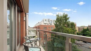 Ein Balkon mit Glastür, Tisch und Stühlen sowie Blick auf die umliegenden Gebäude.