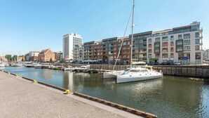 Eine Marina mit vertäuten Booten, eine Uferpromenade und moderne Gebäude im Hintergrund.