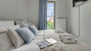 Ein Hotelzimmer mit Bett, Flachbildfernseher, Fenster mit Blick auf ein Gebäude und einem Buch auf dem Bett.