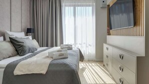Et moderne hotelværelse med seng, fjernsyn, kommode og et vindue med gardiner.
