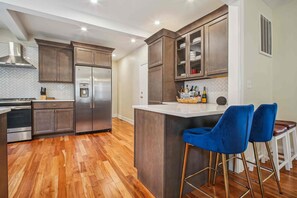 A modern kitchen with stainless steel appliances, wooden flooring, and a bar area with blue bar stools. - Spacious 4-bedroom Single Family home in Historic  Weequahic Newark NJ (Newark)
