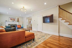 A living room with a sofa, a fireplace, a television, and a staircase. - Spacious 4-bedroom Single Family home in Historic  Weequahic Newark NJ (Newark)