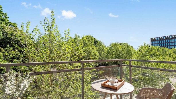 Ein verglaster Balkon mit rundem Tisch, zwei Korbstühlen und einer Ablage mit Tassen und einem Buch.
