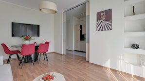 Ein modernes Wohnzimmer mit Essbereich, Holzboden, einem runden Tisch mit roten Stühlen, einem weißen Sofa und einem flachbildfernseher an der Wand.