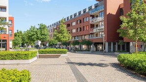 Ein moderner Stadtplatz mit mehrstöckigen Gebäuden, gepflasterten Wegen und Grünflächen.