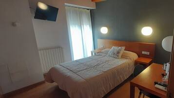A hotel room with a bed, bedside tables, a TV mounted on the wall, and a window with curtains.