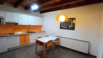 Een kleine keuken met witte kastjes, een magnetron, een spoelbak en een tafel met stoelen.