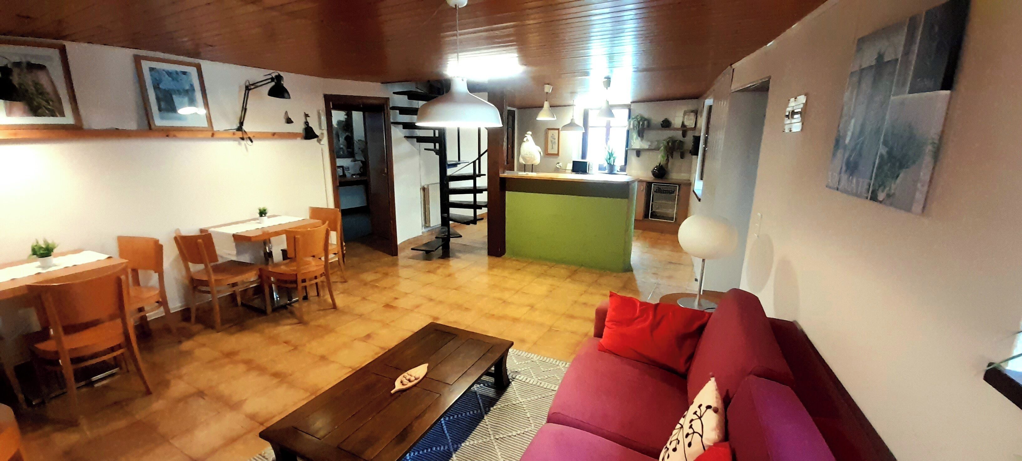 Una sala de estar acogedora con suelo de madera, un sofá rojo, una mesita de centro de madera y un comedor con sillas y una mesa.