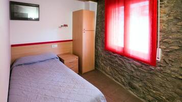 Ein Schlafzimmer mit Bett, Kleiderschrank, kleinem Tisch, Spiegel und einem Fenster mit roten Vorhängen.