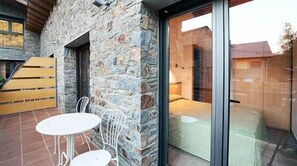 Paredes externas de pedra, porta de vidro e um pequeno pátio com mesa e cadeiras.
