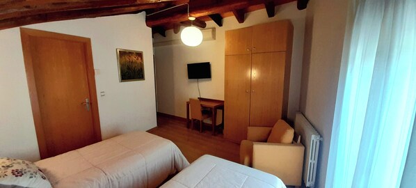 A bedroom with two beds, a desk, a chair, a television, and a wardrobe. - Cal Miquel (Anserall)