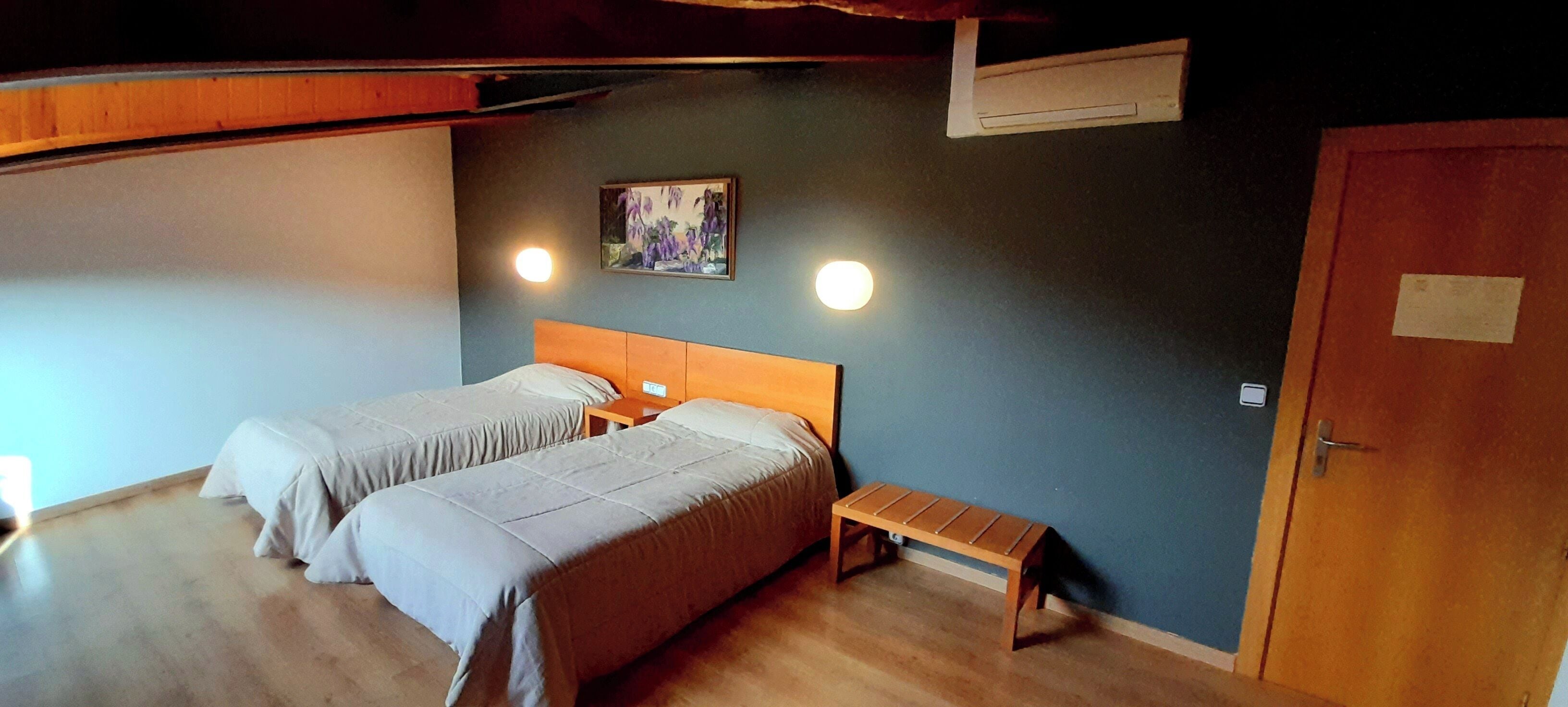 Una habitación con dos camas, un banco, un cuadro y una puerta.