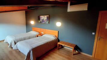 Una habitación con dos camas, un banco, un cuadro y una puerta.