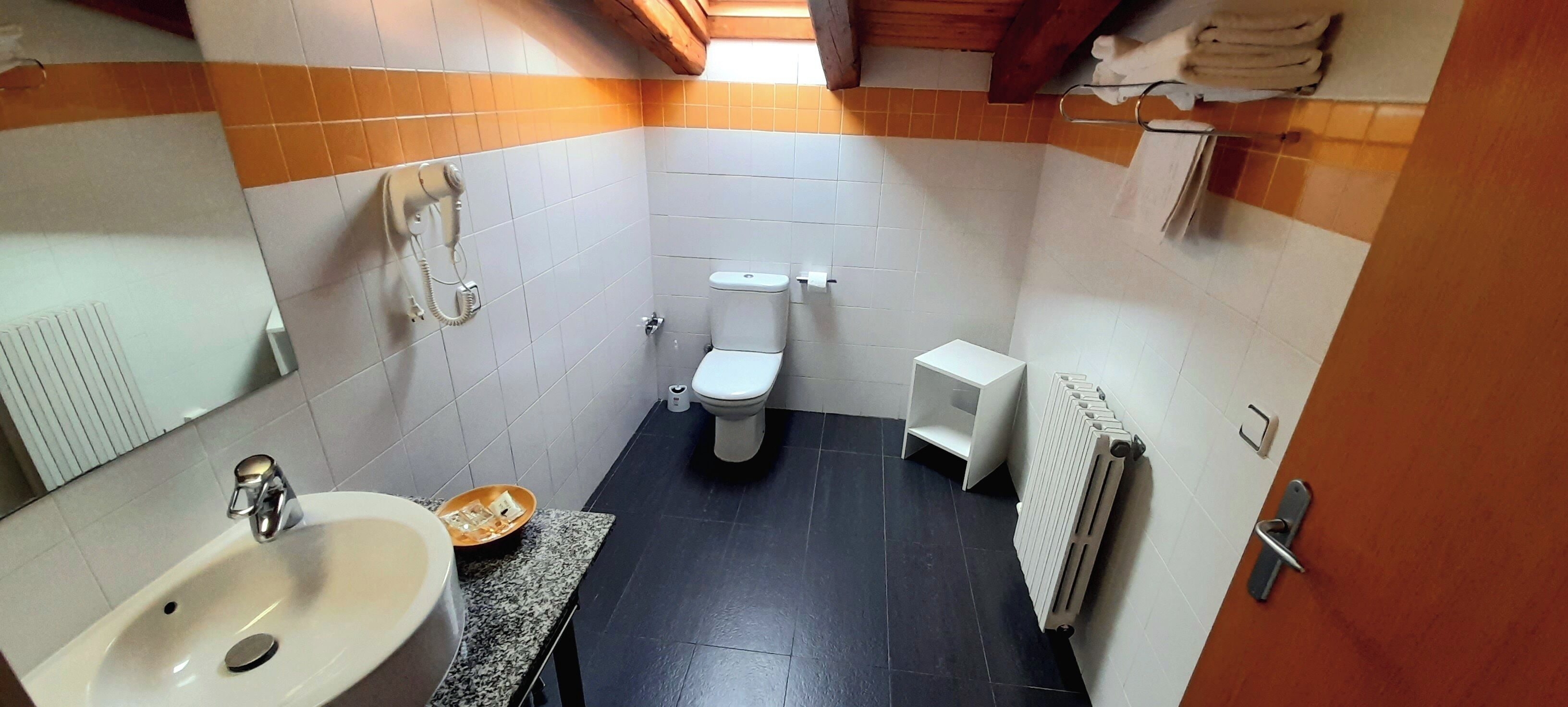 A compact bathroom with a sink, toilet, and a small shelf.