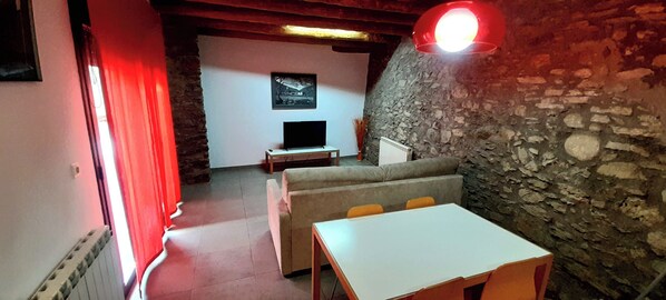 Une pièce confortable avec un mur en pierre, une télévision, un canapé et une table.