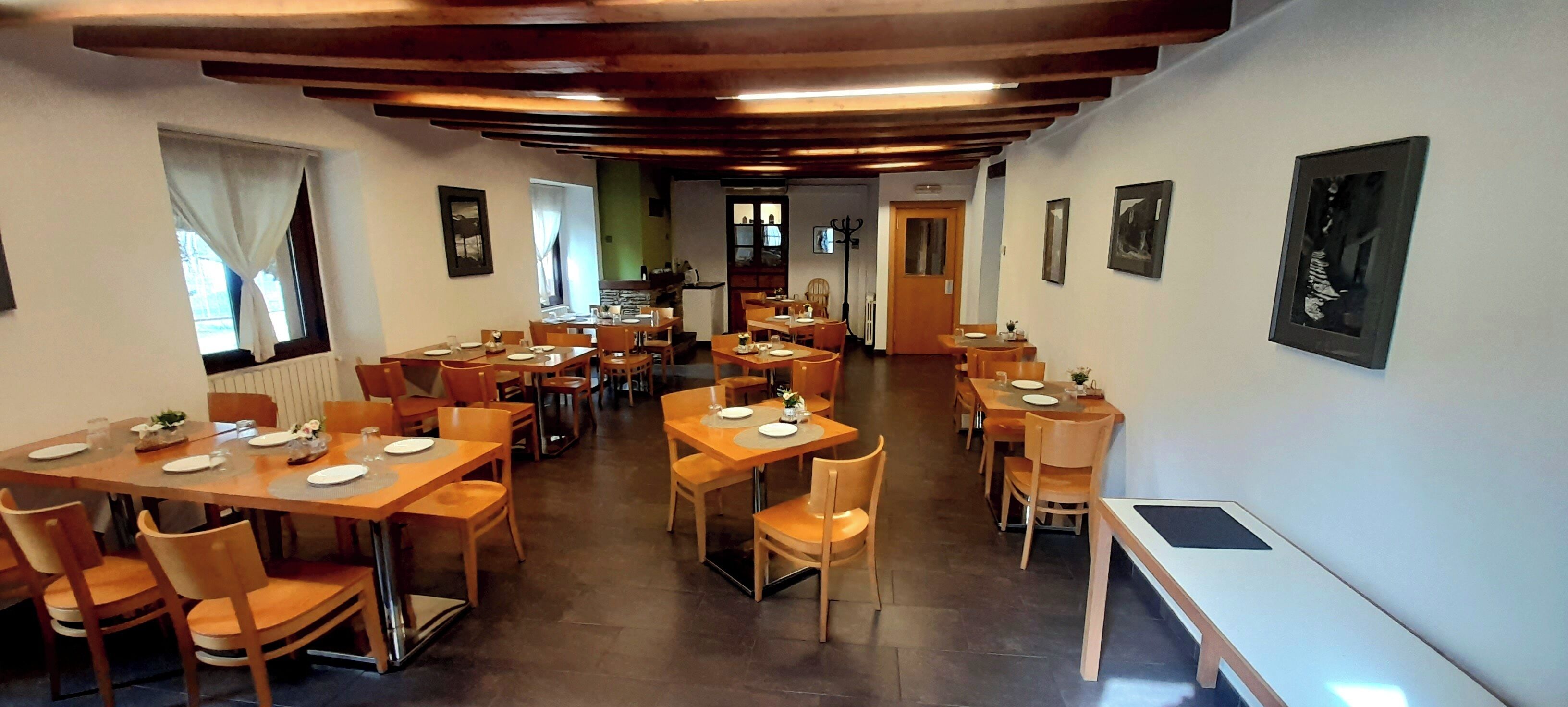 Un restaurante con mesas y sillas de madera, una cocina al fondo y cuadros en las paredes.