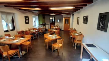 Un restaurante con mesas y sillas de madera, una cocina al fondo y cuadros en las paredes.