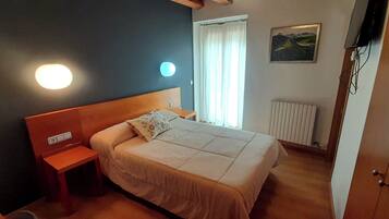 Una camera da letto con un letto, un comodino, una lampada a parete, una finestra con tende e un termosifone.