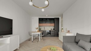 Ett modernt vardagsrum med en platt-TV, en grå soffa, ett träbord med en fruktskål, en matplats med ett vitt bord och stolar samt ett kök med mörka skåp och en vit bänkskiva.