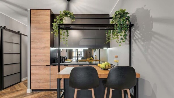Una cocina moderna con encimera de madera, dos sillas negras y plantas colgantes.