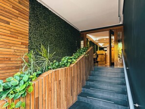 A modern staircase with a wooden handrail and a dark wall with green plants. - Rooftop Pool Studio · Steps from 5th Ave & Beach (Playa del Carmen)