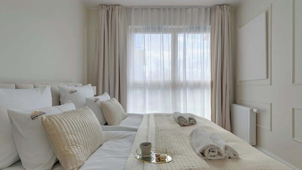 Een hotelkamer met een groot bed, een nachtkastje met dienblad en een raam met gordijnen.