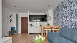 Un salon moderne avec un canapé, une table à manger et des chaises, une cuisine en arrière-plan et un mur décoré de motifs.