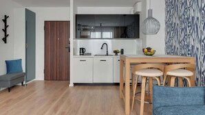 Une cuisine compacte avec des meubles blancs, un four encastré et un coin repas comprenant une table en bois et des tabourets.