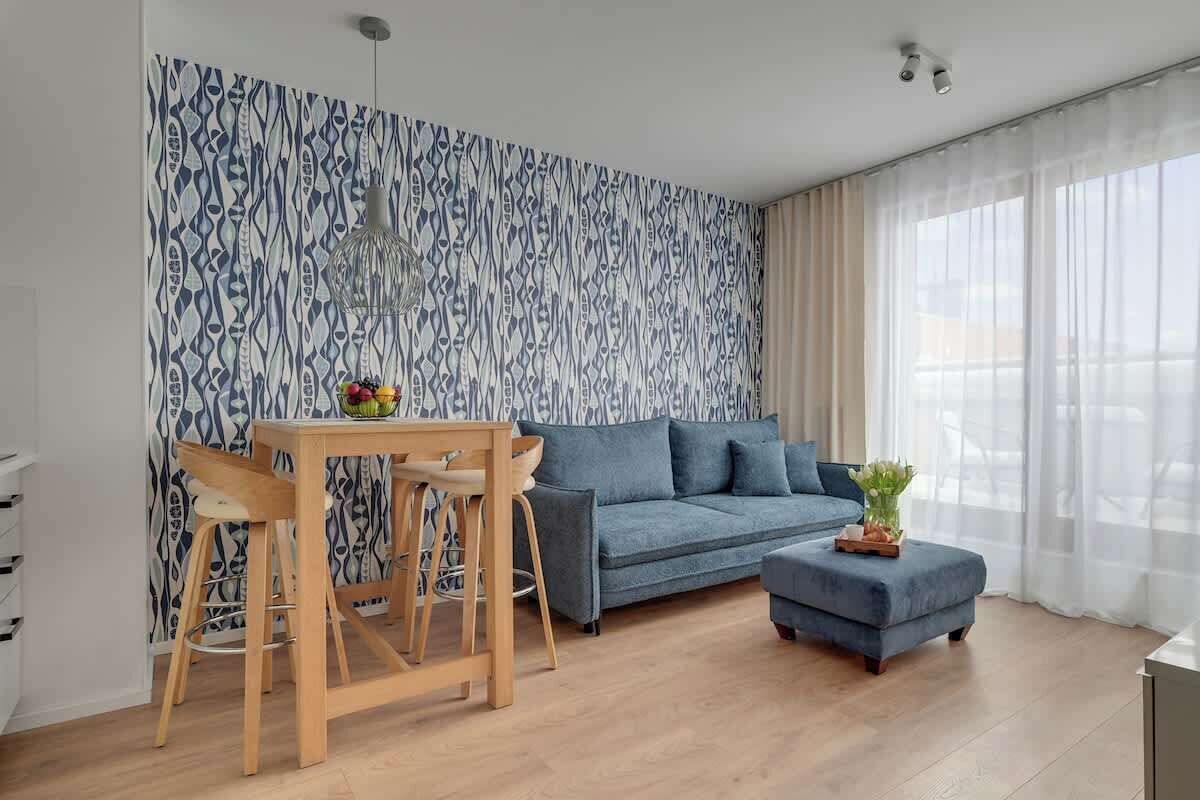 Un salon moderne avec un papier peint à motifs, un canapé bleu, une table à manger en bois avec des chaises et une petite table d’appoint agrémentée d’une plante.
