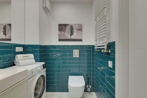 Une petite salle de bain équipée d’un lave-linge, de toilettes et d’un porte-serviettes.