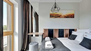 Una habitación de hotel con una cama, un ventanal, un cuadro y una lámpara colgante.