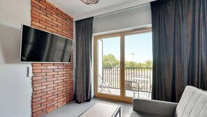 Una sala de estar moderna con un televisor de pantalla plana, una pared de ladrillo decorativa, un sofá gris, una pequeña mesa y un puerta corrediza de vidrio a un espacio al aire libre.
