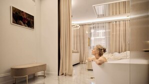 Ett modernt hotellrum med en stor säng, en bänk, en tavla på väggen och utsikt över staden genom fönstret.
