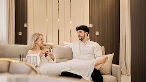 Ett modernt vardagsrum med en soffa, en person som sitter med korslagda ben och en annan person som håller i ett glas.