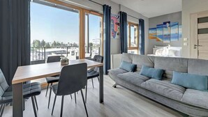 En moderne stue med sofa, spisebord, stole og store vinduer med udsigt over byen.