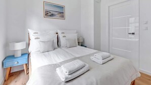 A hotel room with a bed, white bedding, a nightstand with a lamp, a picture on the wall, and a door with a handle. - Nadmotławie C31 | Riverside | Sauna & Gym (Gdańsk)