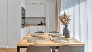 A modern dining area with a wooden table, woven placemats, and a vase of dried flowers. - Nadmotławie C31 | Riverside | Sauna & Gym (Gdańsk)